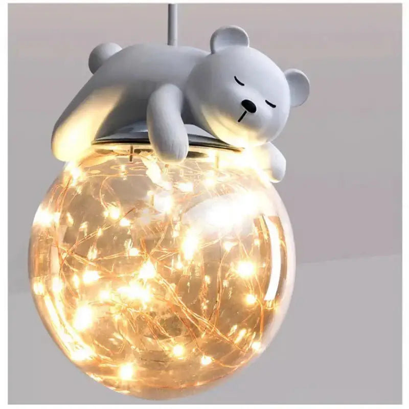 A soft gray plush polar bear atop a glass globe animal led chandelier with warm lights for children’s room lighting