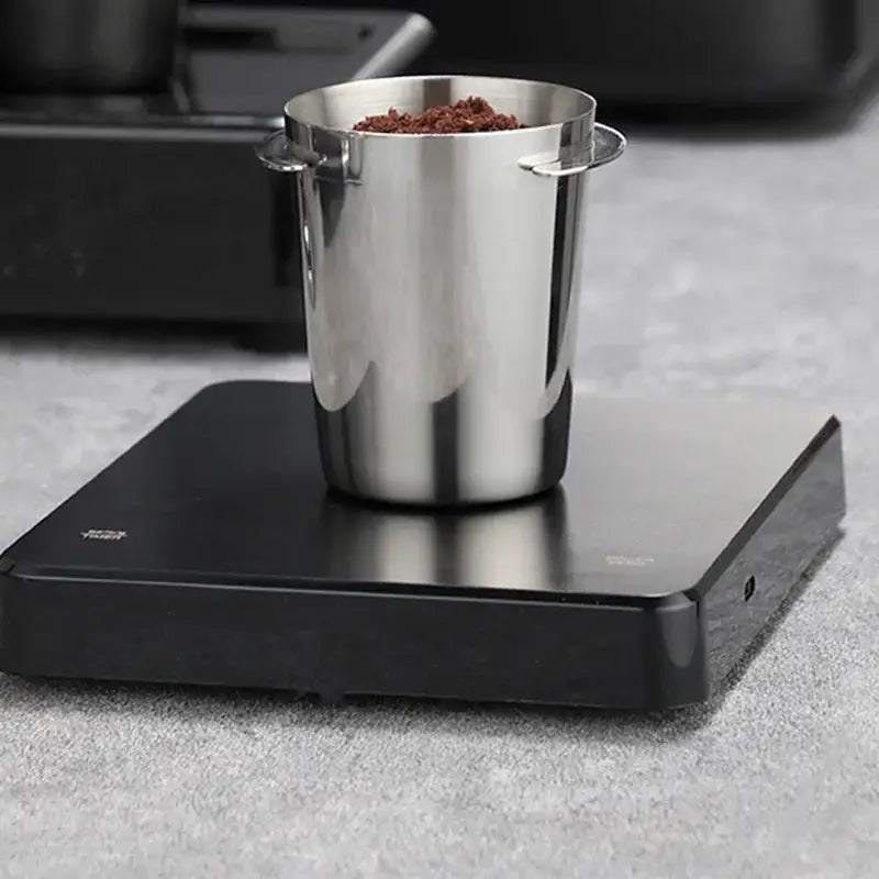 Polished chrome stainless steel espresso dosing cup with two handles filled with ground coffee by decorbites dosing cup