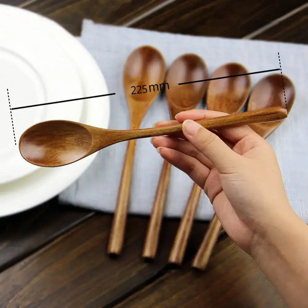 A hand holds a smooth light brown wooden spoon from a polished dark brown wooden spoon soup and fork dining set