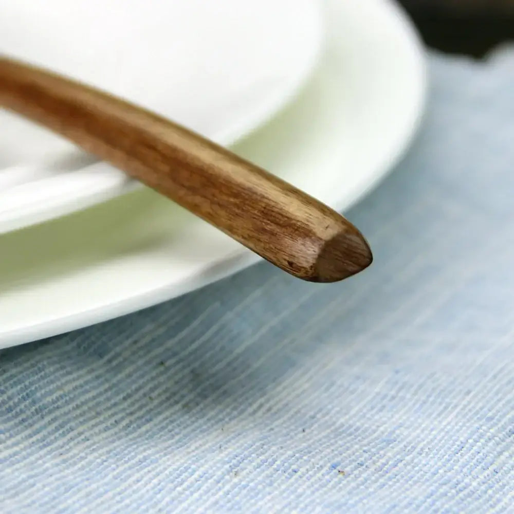 A polished light brown wooden spoon with rounded tip resting on white plate part of a spoon soup wooden spoon set