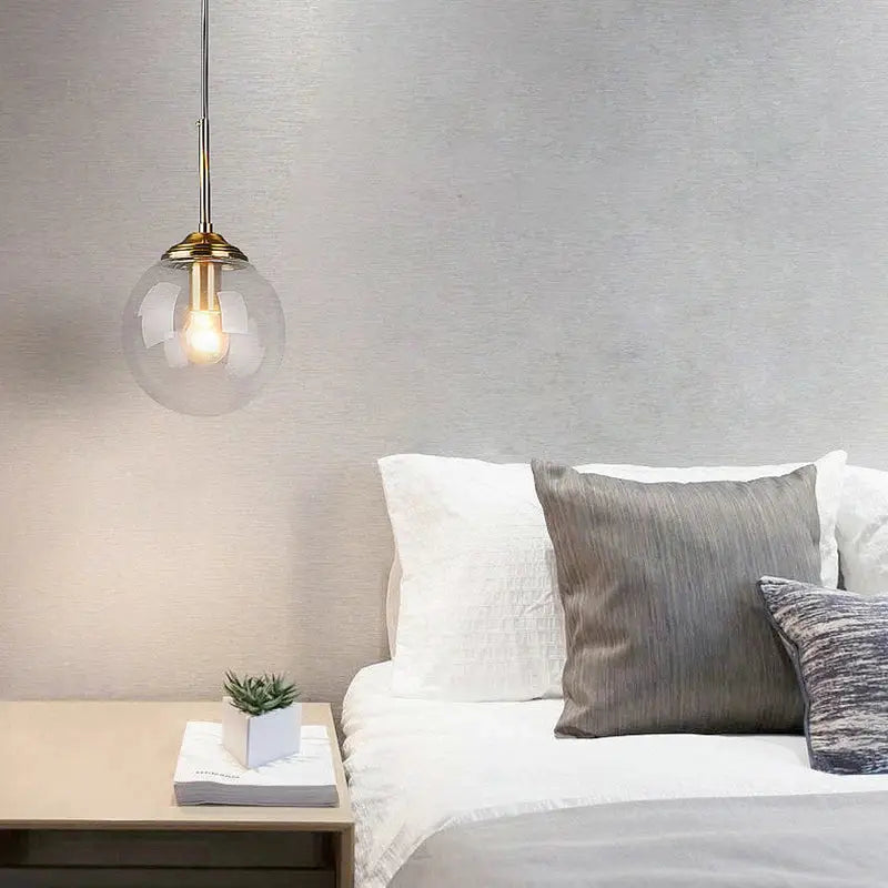 A polished steel glass pendant light with a clear globe and brass accents hanging above the bed