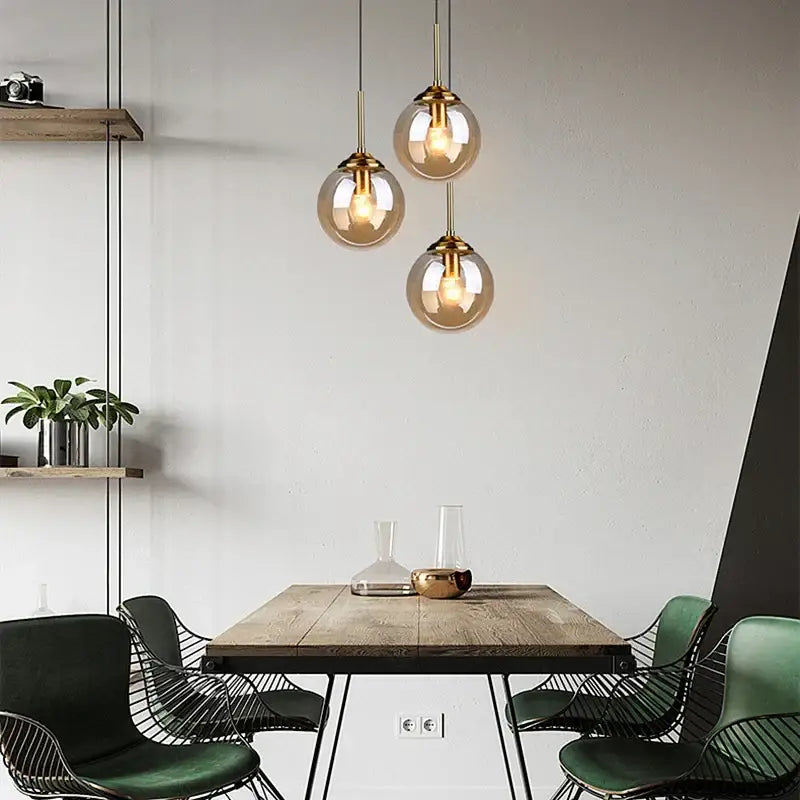 Three polished steel glass pendant lights with brass fixtures hang above a wooden dining table for dining room use