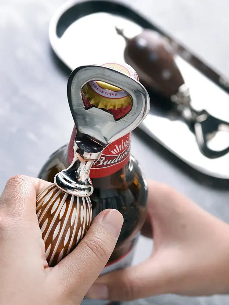 A polished silver beer bottle opener with a wooden striped handle gripping a Budweiser beer bottle for enhanced drinking experience