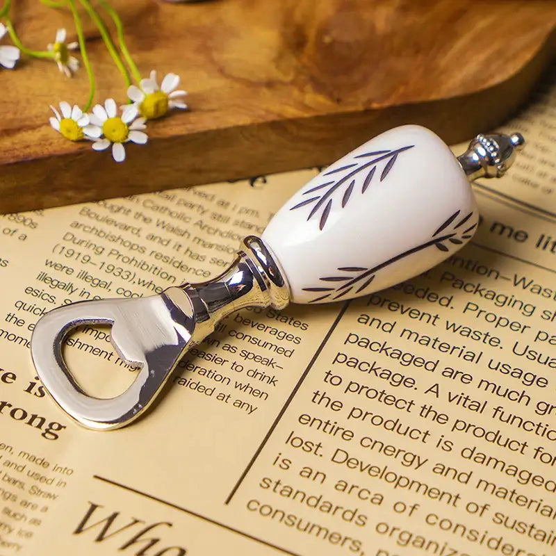 White ceramic beer bottle opener with silver accents and leaf pattern resting on an open book for kitchen use