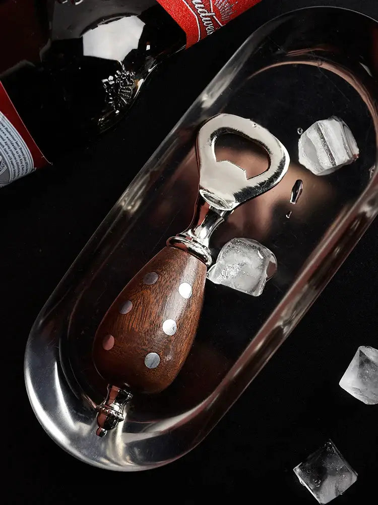 A sleek beer bottle opener with a silver tone and wooden handle featuring white polka dot inlays kitchen tool