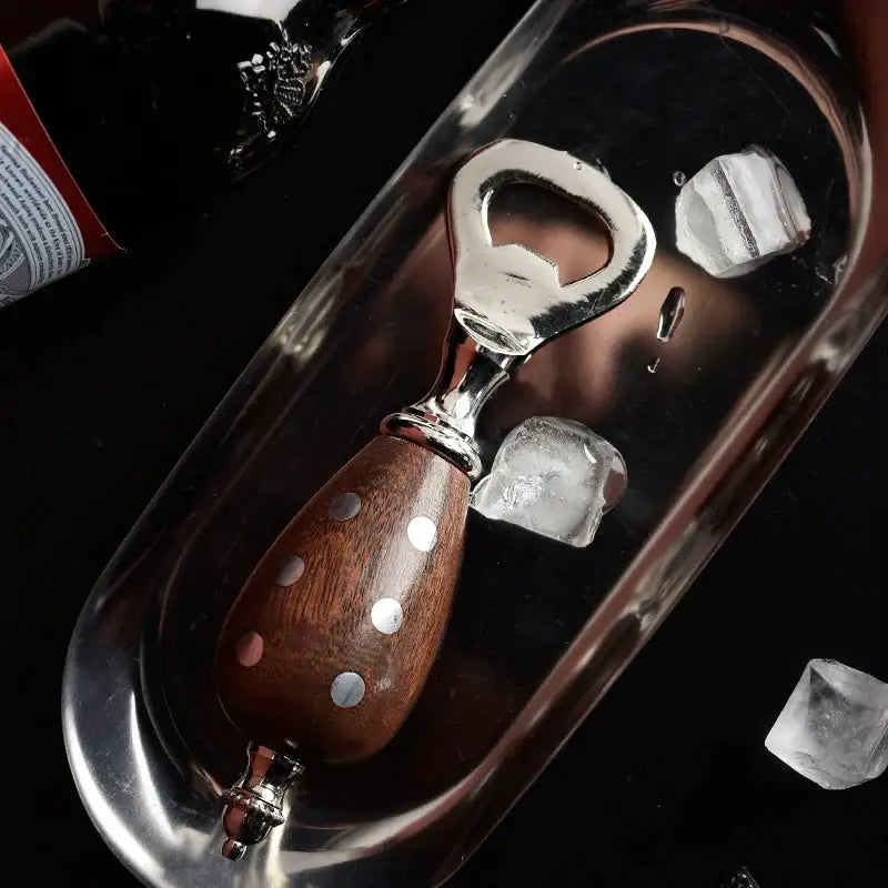 A sleek beer bottle opener with polished wooden handle and silver dots, resting beside ice cubes in a reflective tray