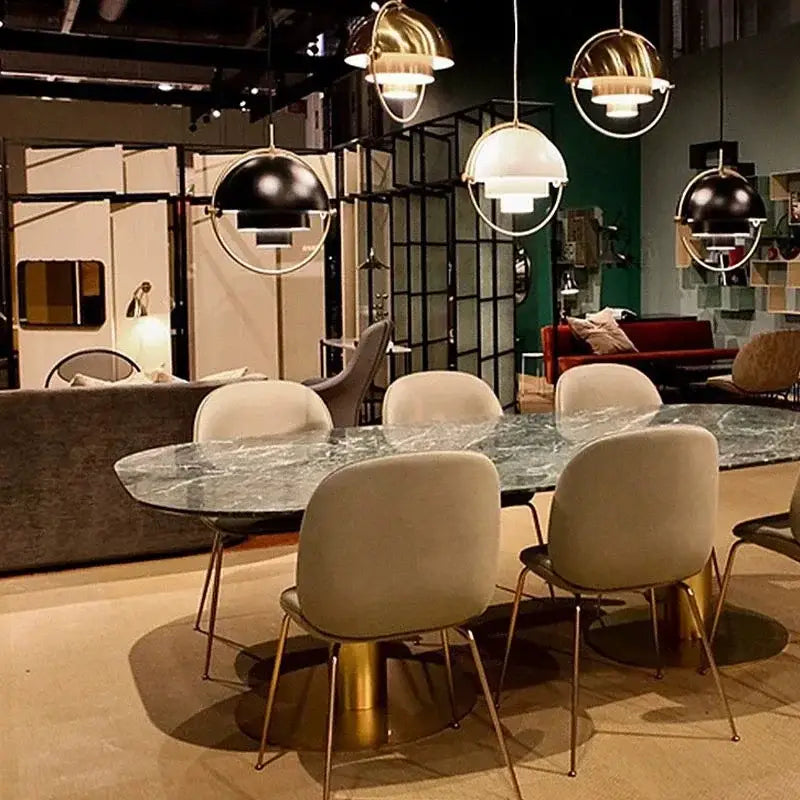 Post modern black and gold iron pendant lights above a gold-toned metal dining table with dark green marble top and legs