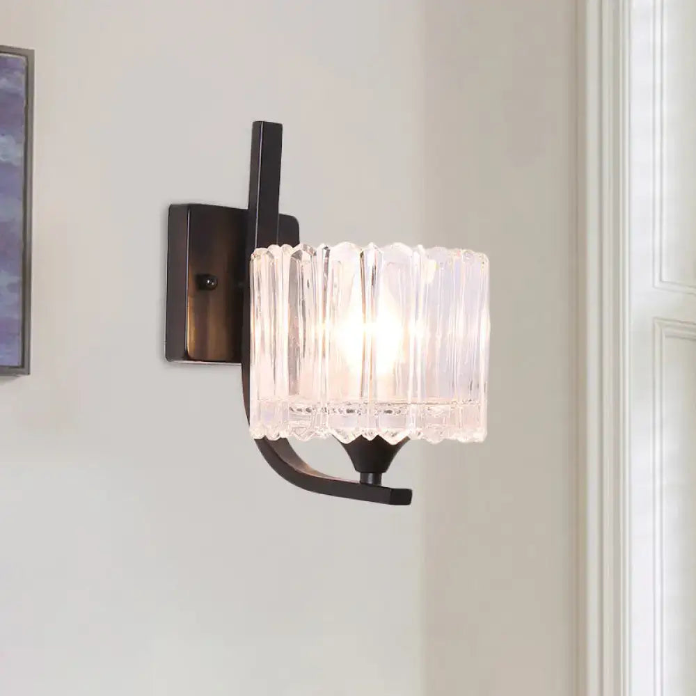 Post-modern black metal wall sconce with a clear crystal shade featuring a vertically ribbed glass design for bedroom use