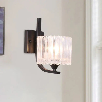 Post-modern black metal wall sconce with a clear crystal shade featuring a vertically ribbed glass design for bedroom use