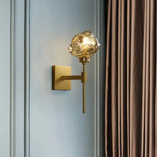 Post modern brass wall light sconce with gold-toned finish and textured frosted amber glass globe for living room use
