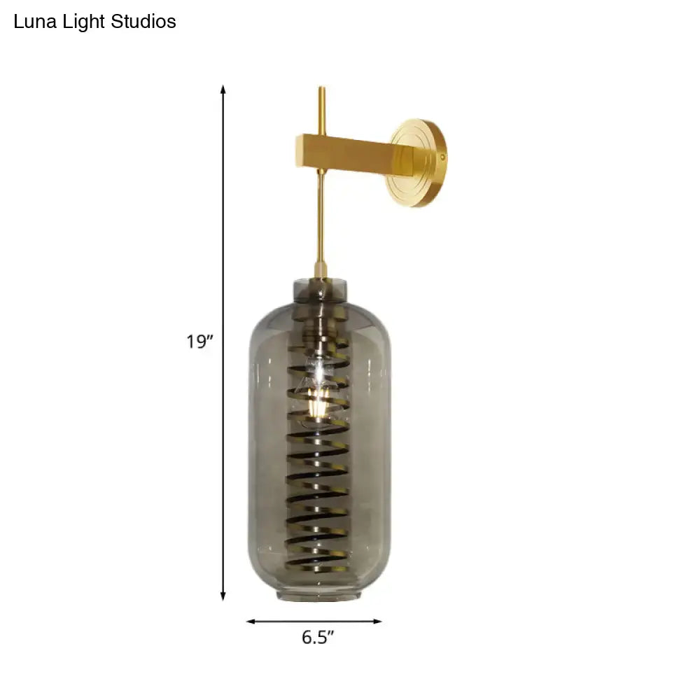 Post-modern brass wall sconce with smoke gray glass cylinder and coiled black spiral design for bedroom lighting