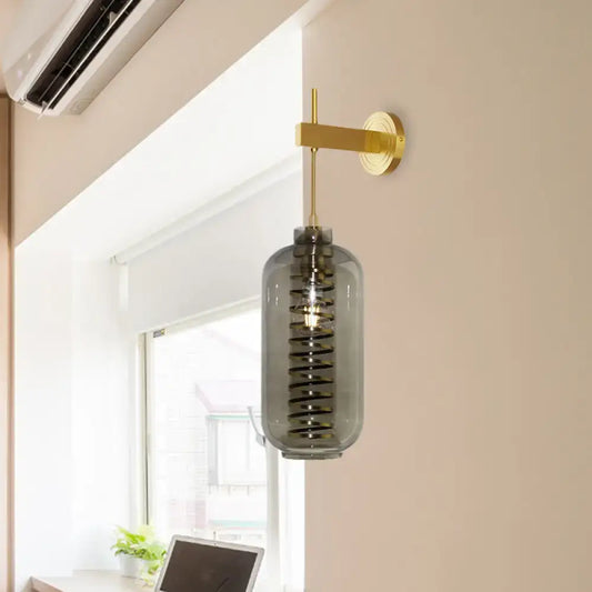 A post-modern wall-mounted brass sconce with smoke gray glass cylinder and internal spiral design for bedroom light