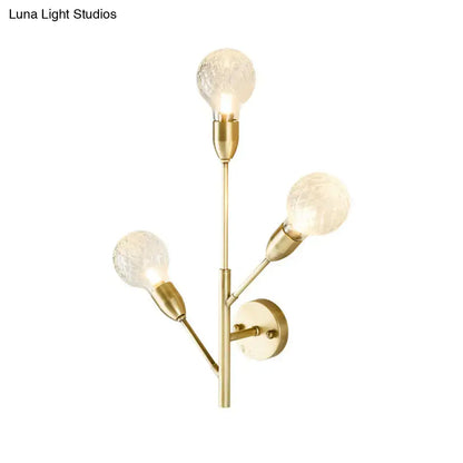 Gold-toned post-modern brass wall light fixture with three clear lattice glass textured bulbs for bedroom use