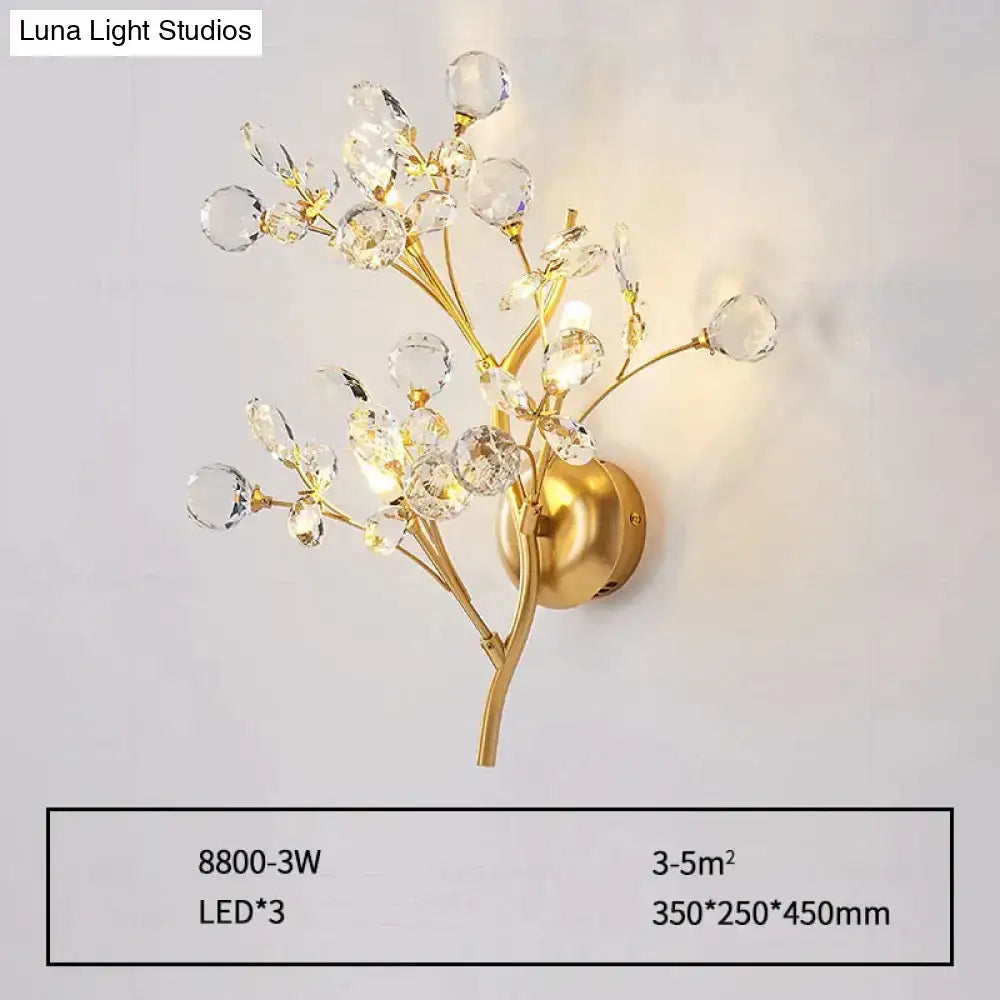 Post modern luxury gold-toned wall sconce with crystal branches and spherical accents for bedroom lighting
