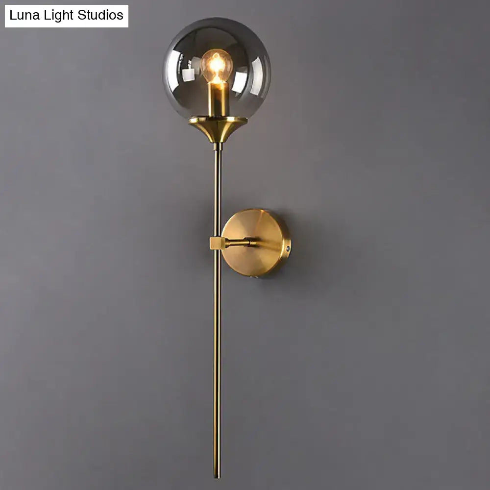 A sleek brass postmodern wall sconce with smoke grey glass and an exposed e27 bulb for bedroom use