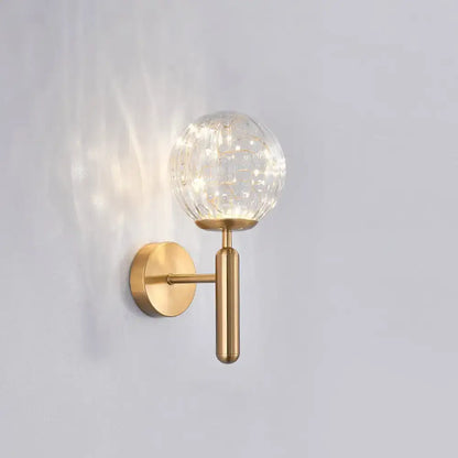 Gold-toned postmodern wall sconce with textured clear prismatic glass shade for modern style bedroom lighting