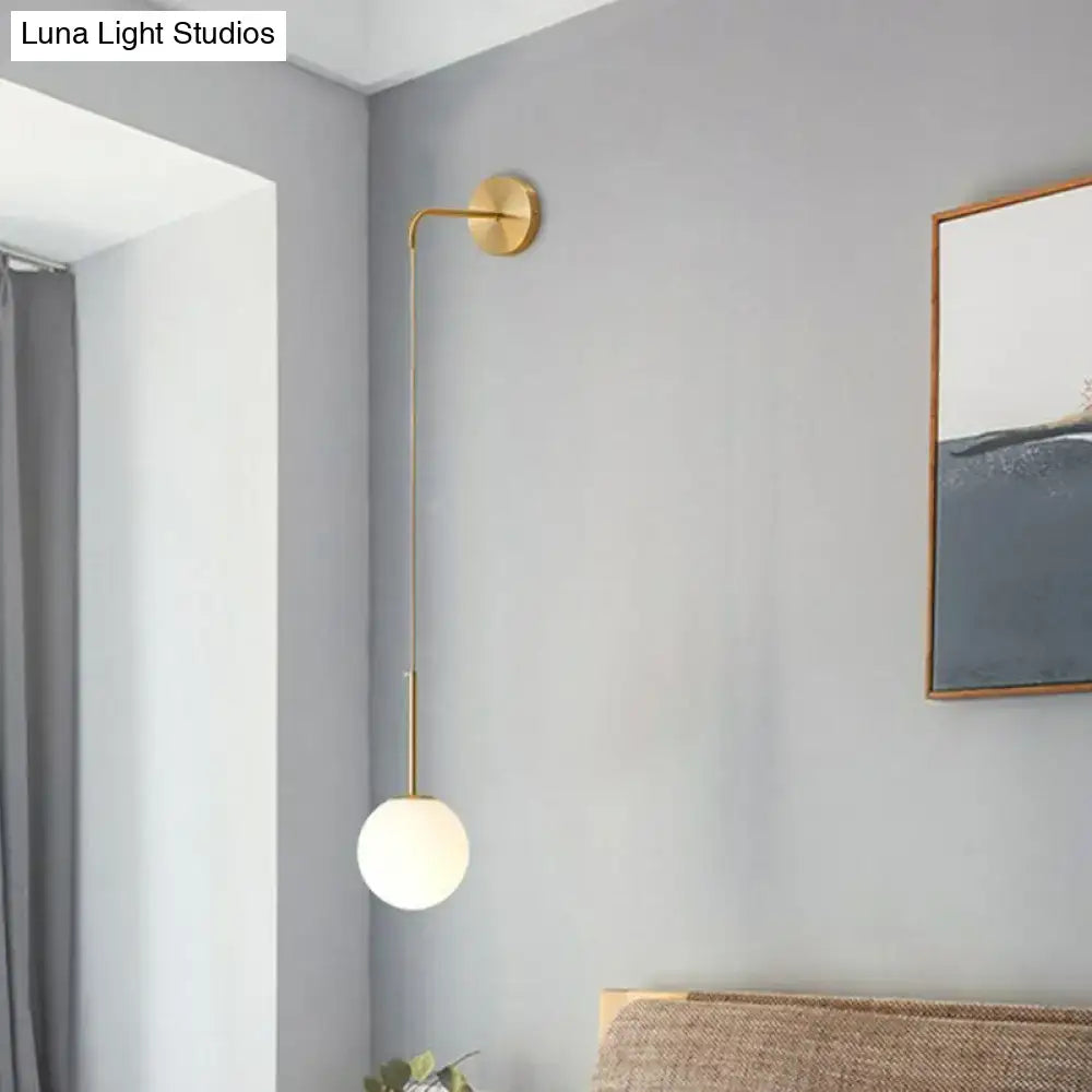 Gold-toned minimalist wall lamp with slender curved arm and frosted glass globe shade for bedroom use