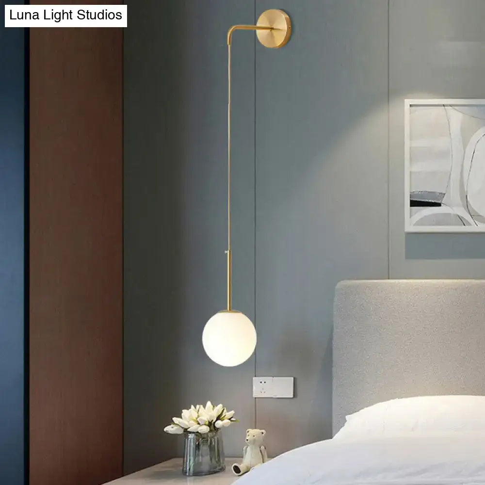 Gold-toned wall lamp with slender curved arm and frosted glass globe for bedroom in postmodern style