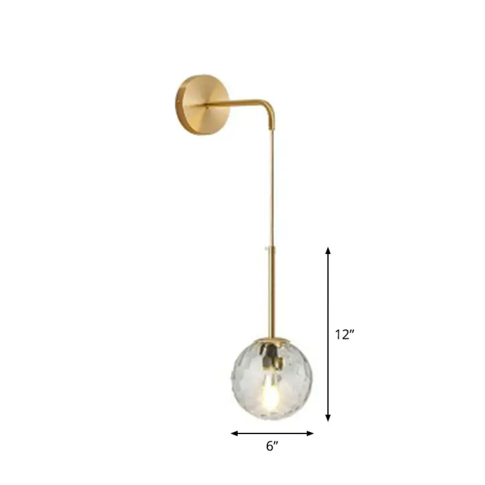 A sleek polished brass wall lamp with a curved arm and faceted crystal globe shade for elegant bedroom lighting