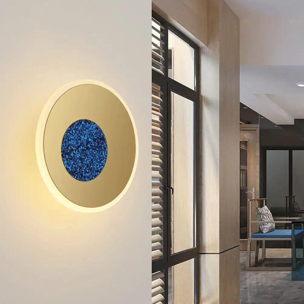 Postmodern blue round sconce light fixture with gold-toned outer ring and glittery blue inner circle for bedroom use