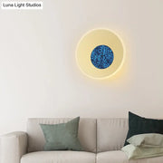 Postmodern blue round sconce light fixture with glowing cream ring and textured sparkling blue center for bedroom use