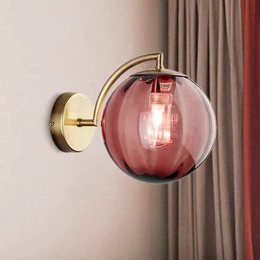 Postmodern brass armed ball sconce with amber glass globe and brass mounting plate for bedroom wall lighting