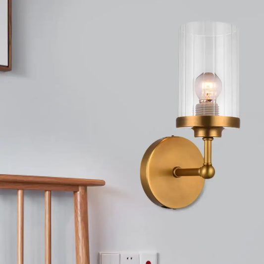 Postmodern brass wall light with clear ribbed glass cylinder housing an exposed bulb for bedroom use