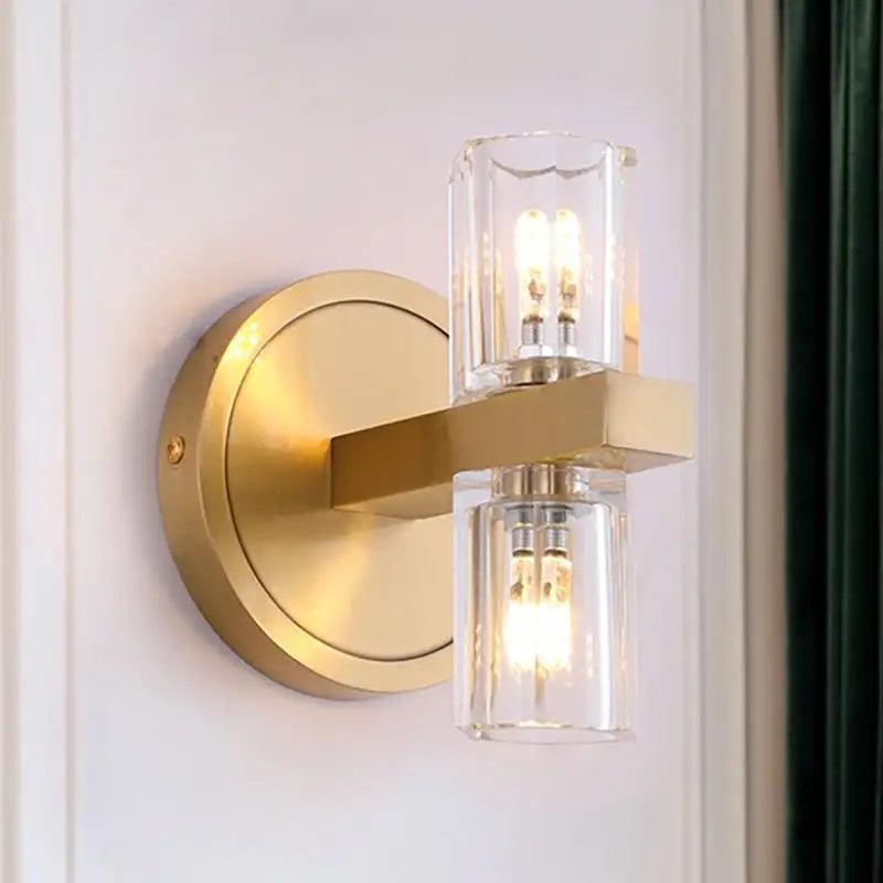 Gold-toned postmodern wall light with brass finish and two clear glass cylinders highlighting fixture height for bedroom use