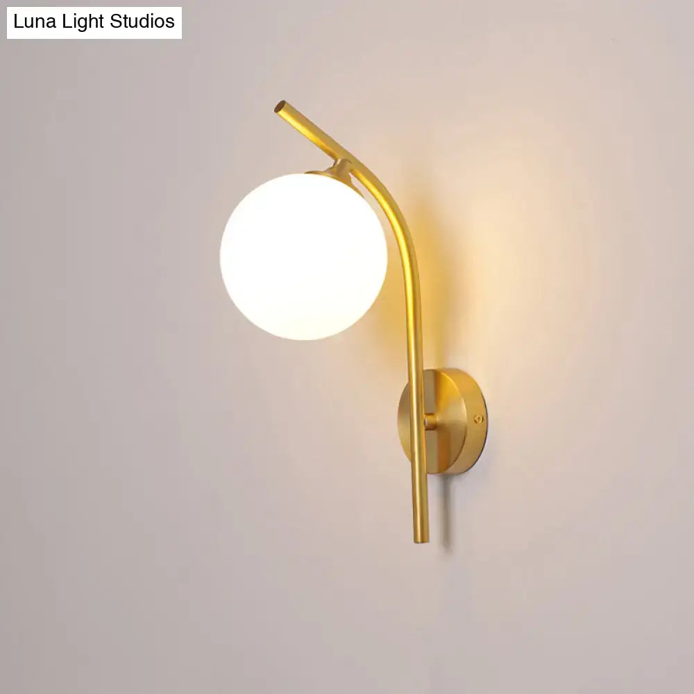 Postmodern brass wall sconce with a gold-toned curved arm and white glass geometric frosted globe shade for living room