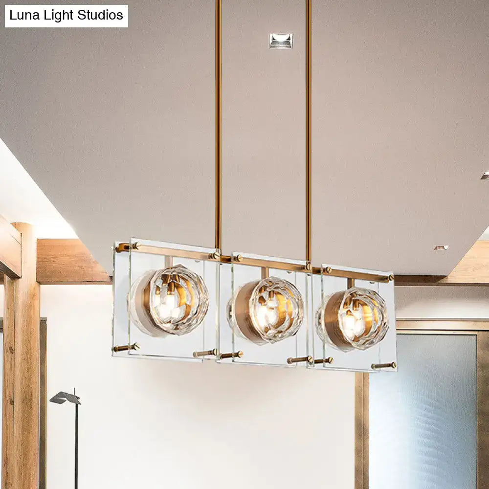 Modern kitchen island light with three faceted crystal globe shades and a brass-finished metal frame in gold and clear glass