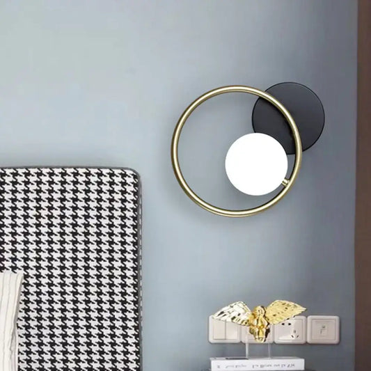 Modern postmodern gold and black ring wall mounted light with circular frame, black disc, and white spherical bulb for bedroom sconce