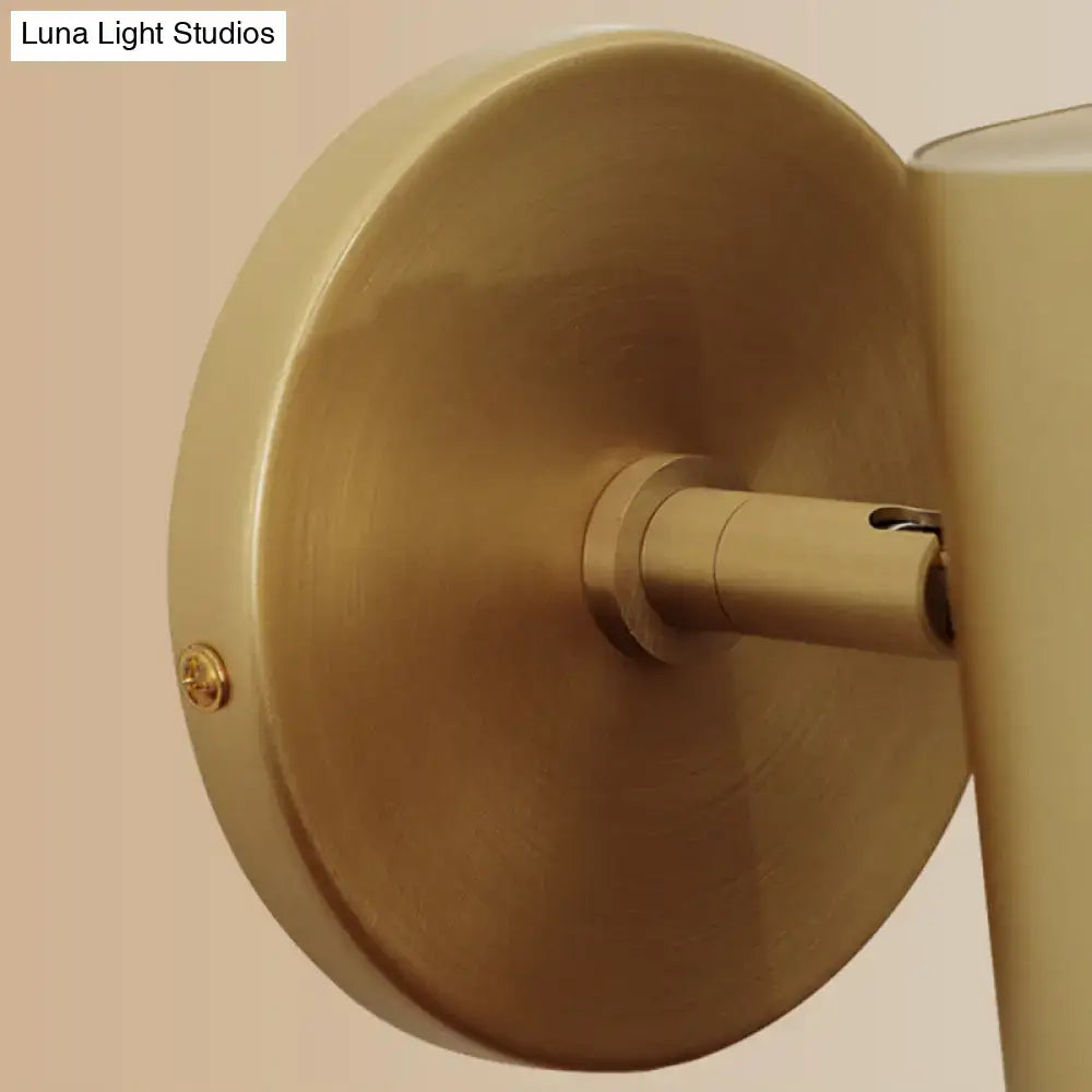 Brass-finished postmodern wall light with circular backplate and cylindrical arm mounted fixture for bedroom reading