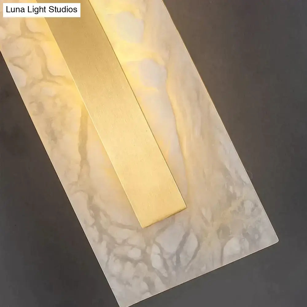 Modern wall lamp featuring a polished brass center with warm light and a white gray copper marble wall backplate