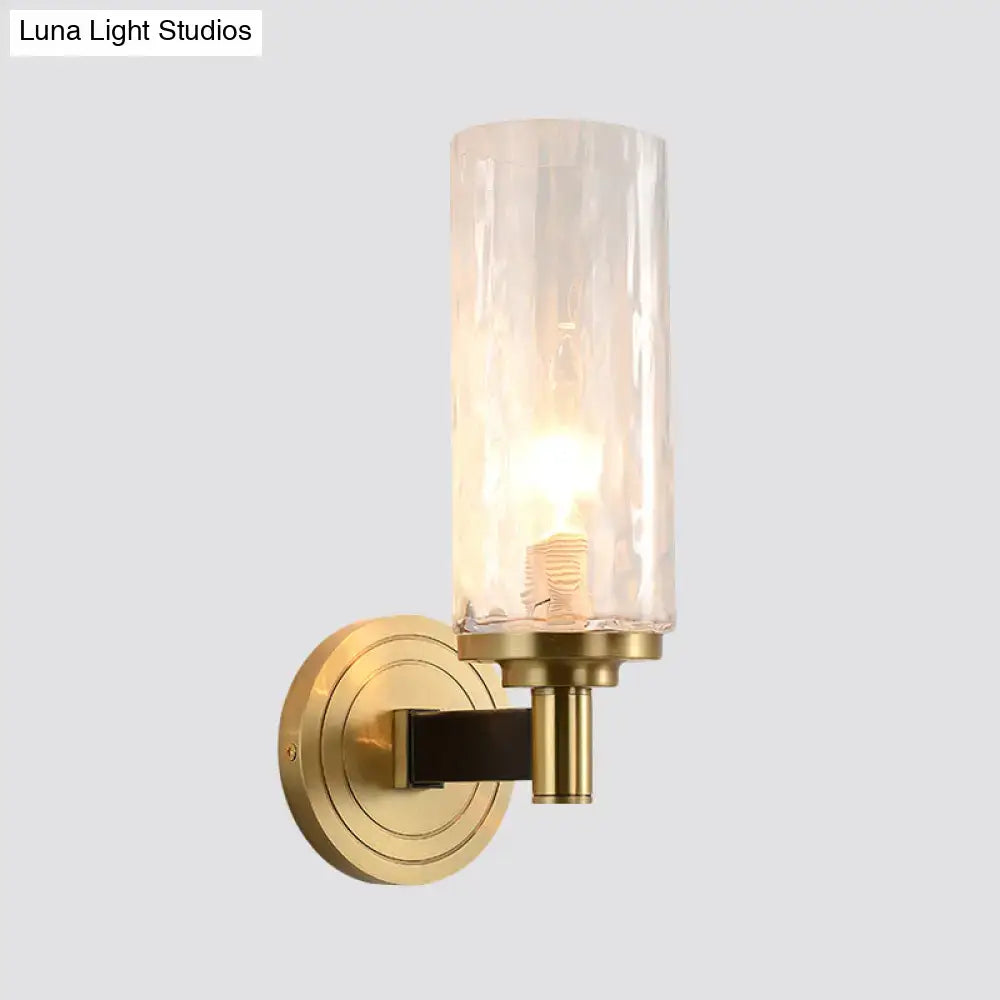 Brass-finished postmodern gold crystal wall mounted light with textured translucent glass cylinder housing illuminated bulb