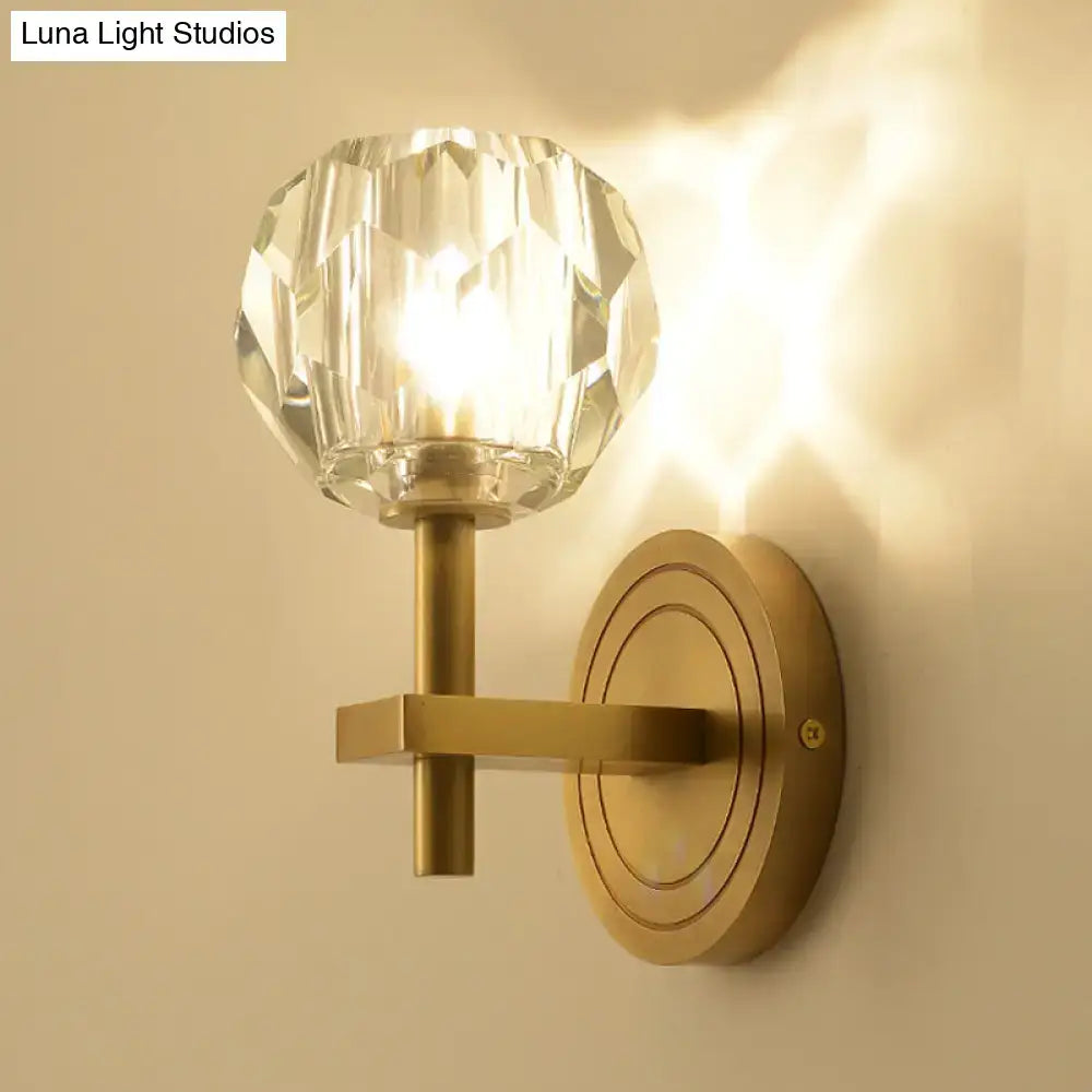A warm-toned brass postmodern wall mounted light with a faceted crystal globe shade for living room decor