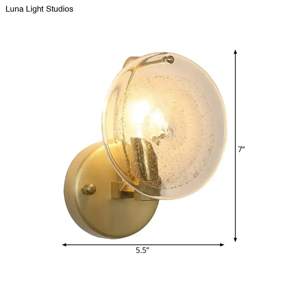 Postmodern brass-finished wall sconce with a clear glass shade featuring subtle internal bubbles for bedroom lighting