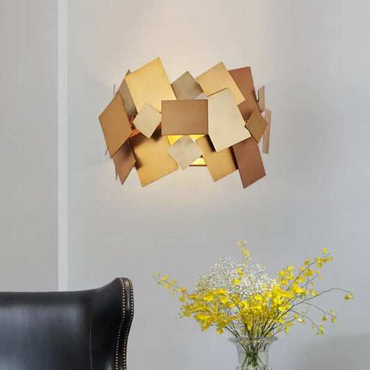 Modern gold-toned postmodern sconce light fixture with overlapping geometric metal plates for living room use