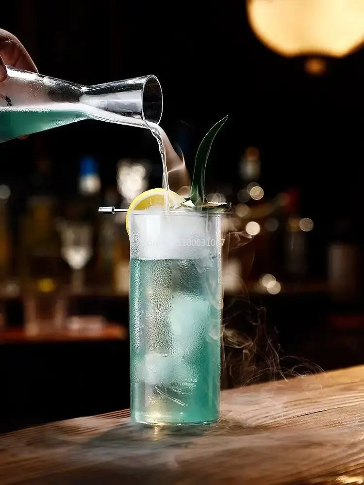 A tall clear glass highball cup filled with a blue cocktail garnished with lemon and green sprig from a highball cup set