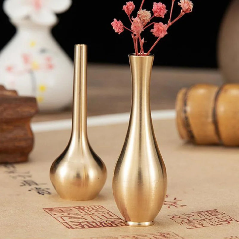 Golden brass mini vintage vases with slender necks and rounded bases one holding dried pink flowers for home decor