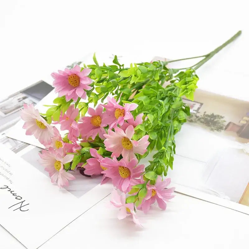 A bouquet of artificial pink daisies with yellow centers and green foliage in a green plant synthetic arrangement