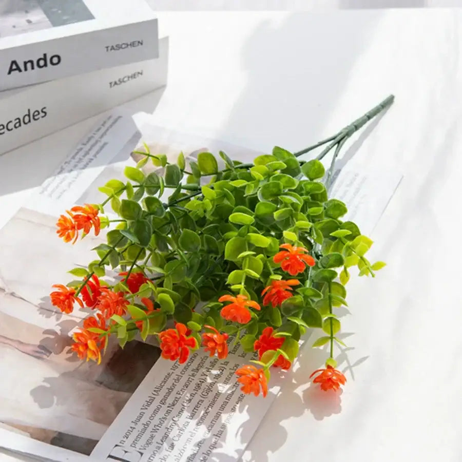 A vibrant orange artificial flower bouquet with lush green leaves made from synthetic material for decorbites artificial eucalyptus plant decor