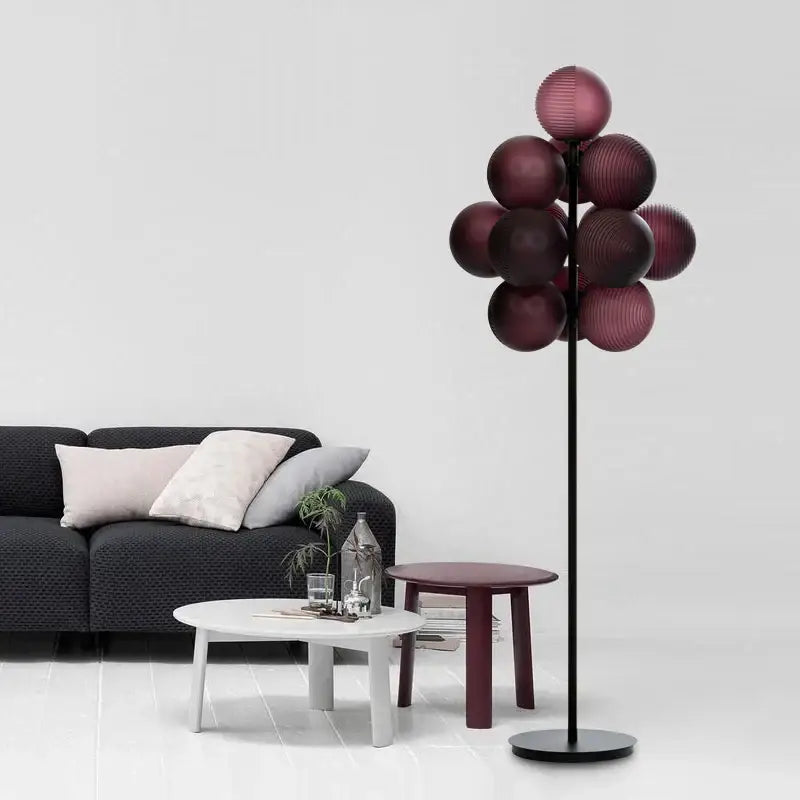 A modern floor lamp with a slender black stand and multiple deep burgundy glass shades in decorbites grape chandelier style