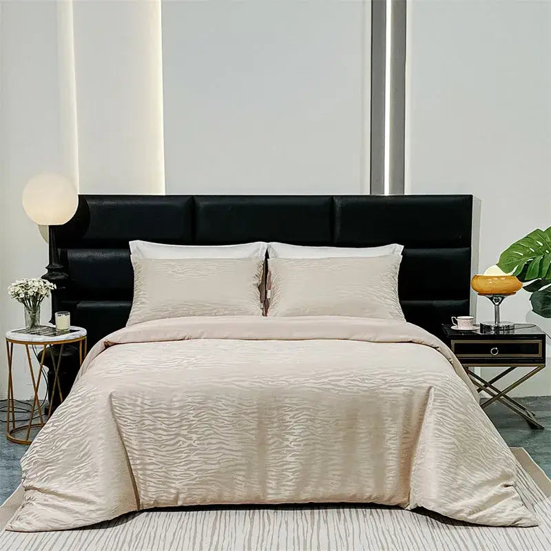 Beige satin duvet cover set with subtle wavy texture displayed on bed with matching pillows and black leather headboard