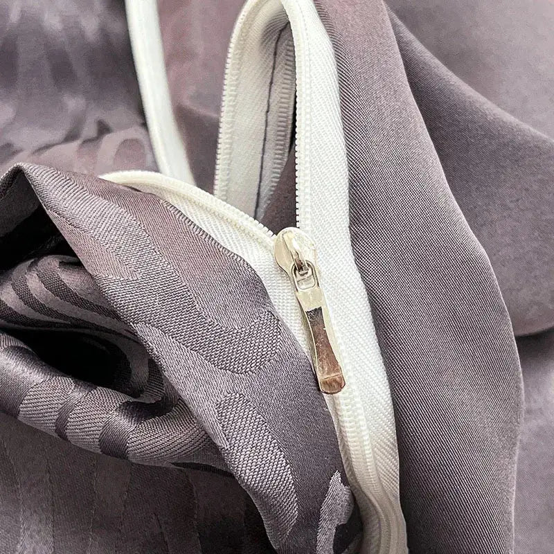 A close-up of a gray satin duvet cover set with subtle geometric patterns and an off-white zipper pull