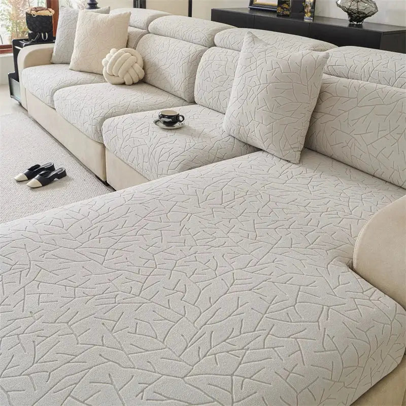 Beige quilted sofa cover with subtle leaf embossed pattern and elastic edges for living room use
