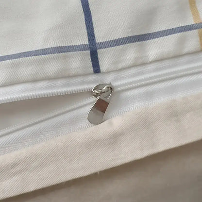 A silver-toned zipper on a quilted cream and black geometric printed bed set with subtle blue and yellow striped fabric