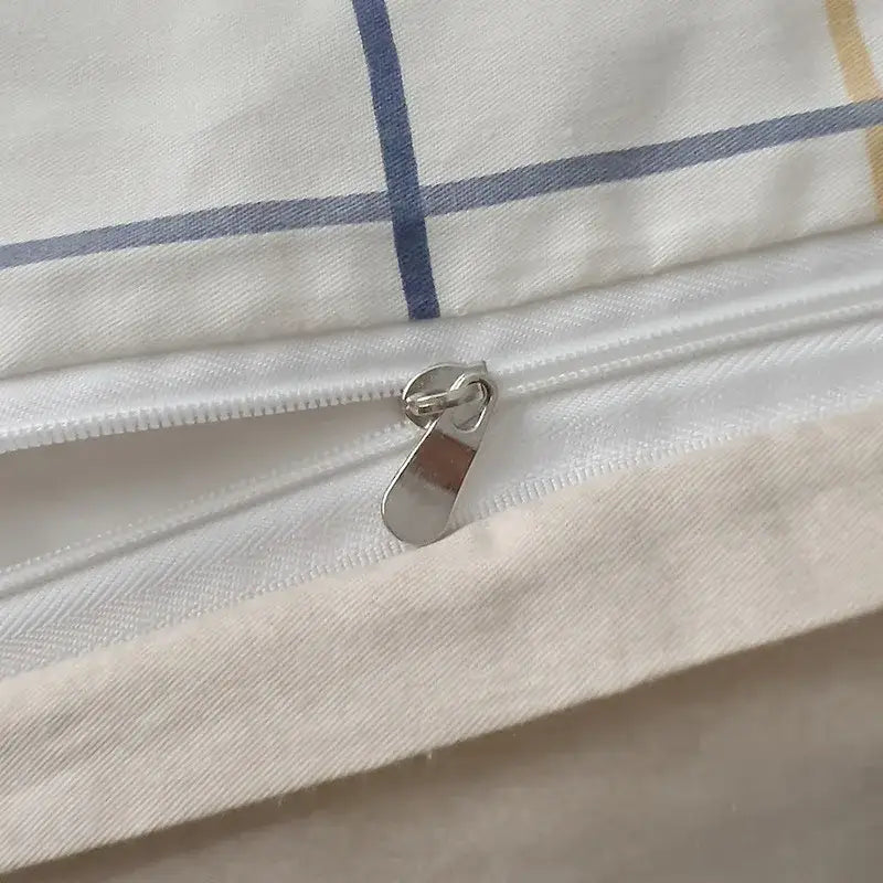 A silver-toned zipper on a quilted cream and black geometric printed bed set with subtle blue and yellow striped fabric
