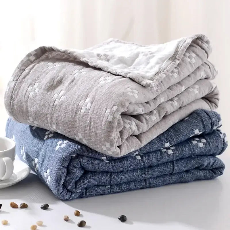 Stacked quilted gray and blue decorbites cotton summer blankets with subtle white geometric patterns on textured fabric