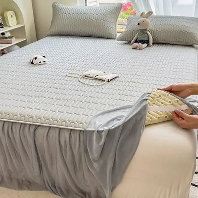 Gray quilted mattress pad with ruffled edge and elasticized border paired with a pink bed skirt set with silver trim