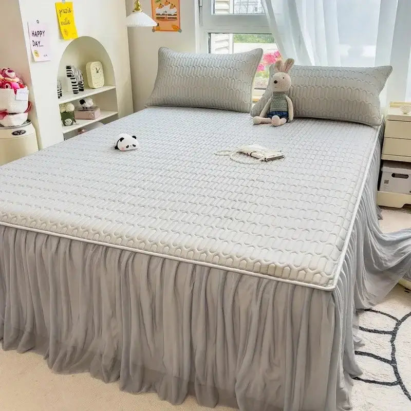 Gray quilted bed pad with stitched wave pattern and ruffled skirt as part of a bed skirt set with silver trim